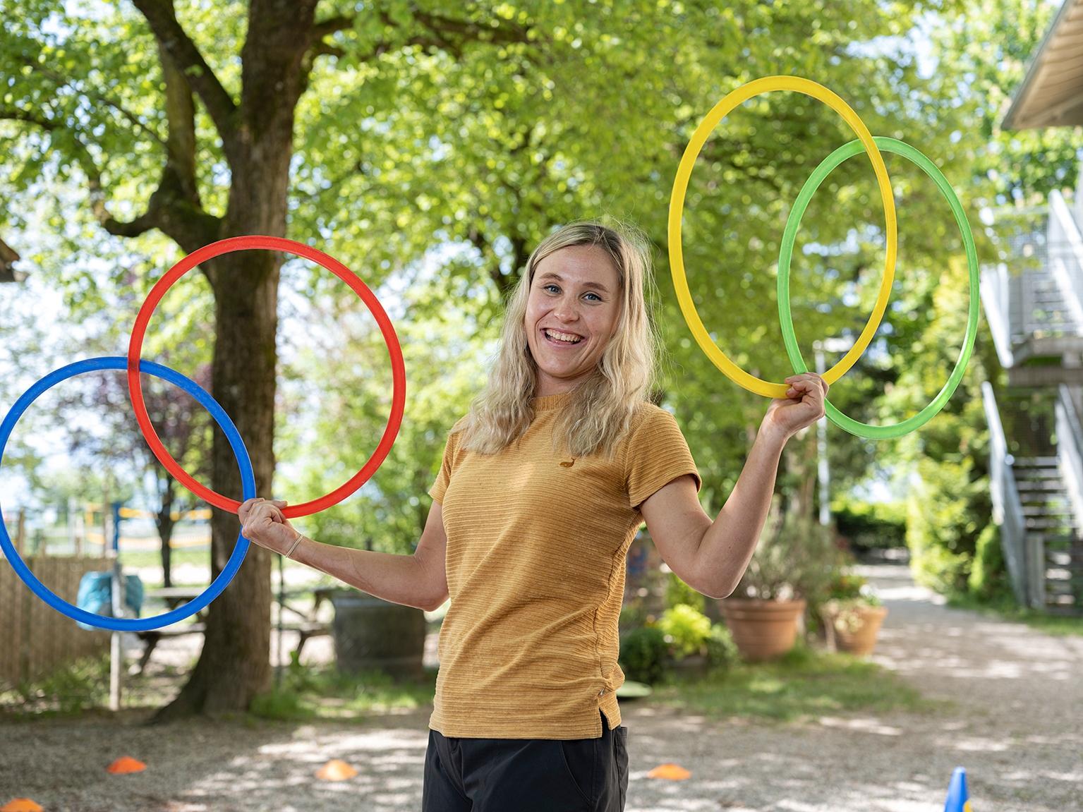 Sportliche Frau steht draußen mit Hula Hoop Reifen in den Händen.