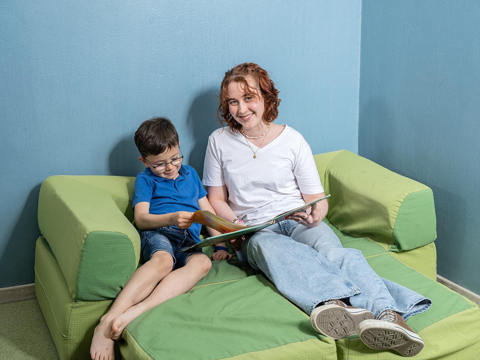 Eine Frau sitzt lesend mit Ihrem Kind gemütlich auf dem Sofa.